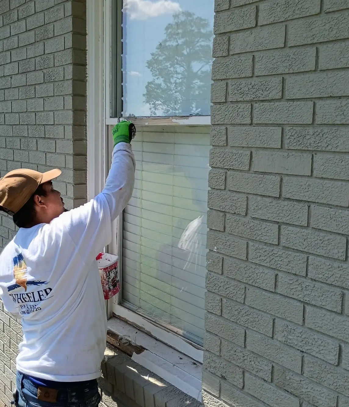 Wheeler Painting crew member brushing white trim on a brick exterior window