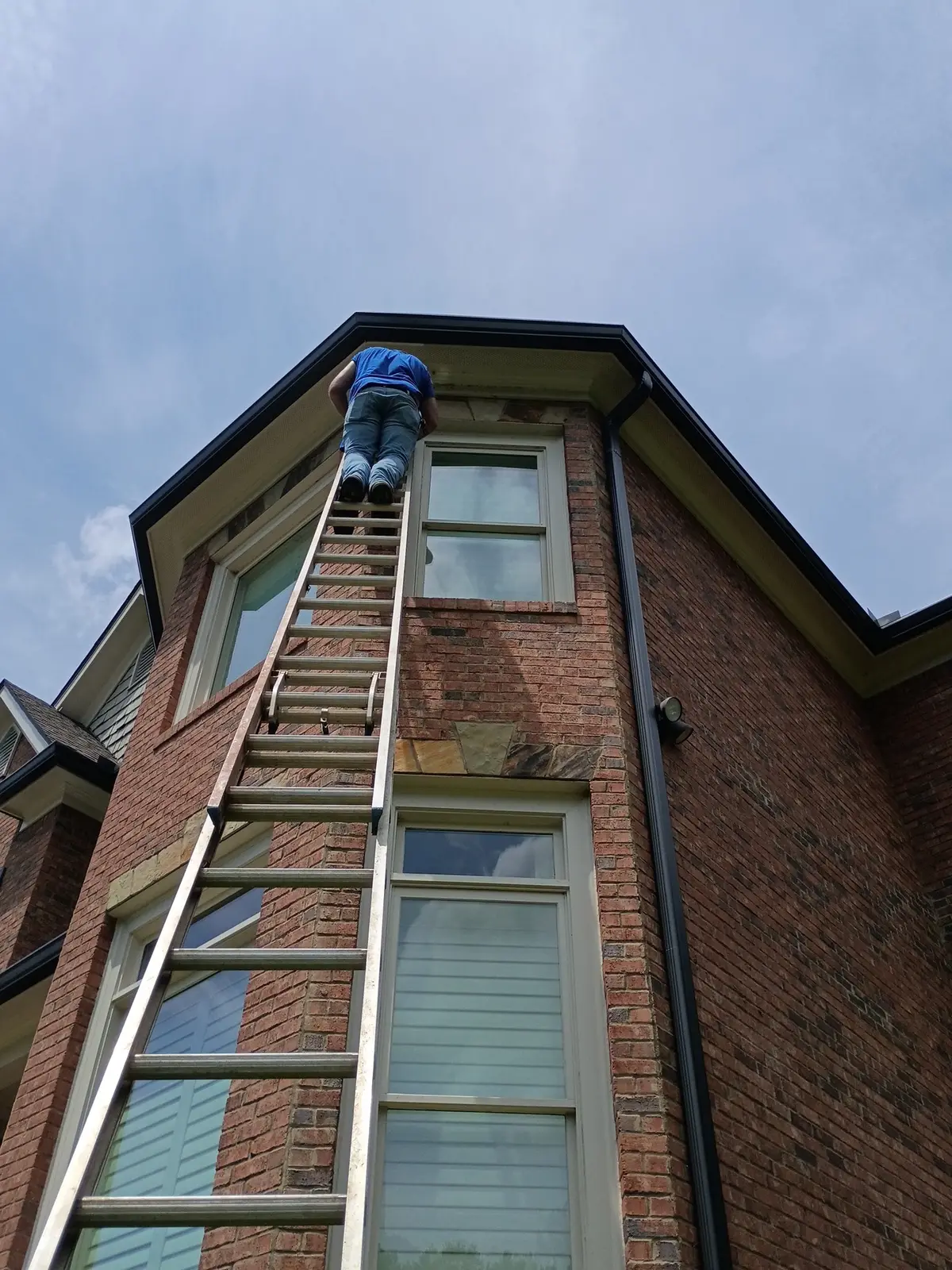 Painter on a tall extension ladder working exterior trim on a brick home