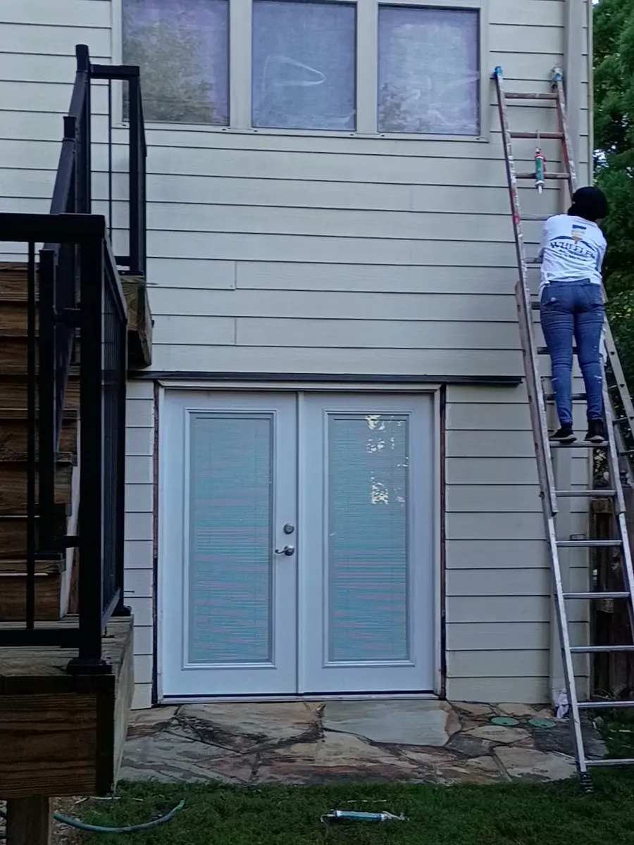 Wheeler Painting crew member on an extension ladder caulking exterior trim before painting