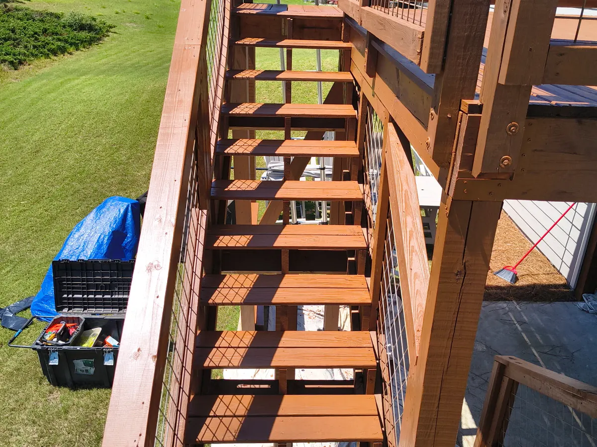 Freshly stained deck stairs with cable railings and job-site tools nearby